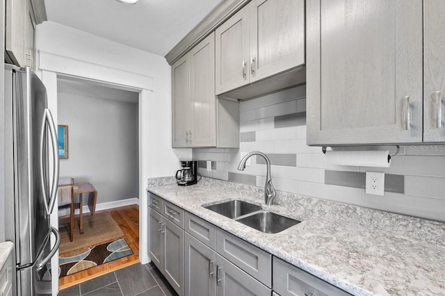 kitchen featuring stainless steel refrigerator, light stone countertops, sink, and tasteful backsplash