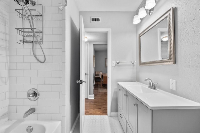 bathroom with hardwood / wood-style flooring, tiled shower / bath, and vanity