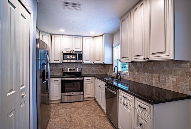 kitchen with tasteful backsplash, sink, dark stone countertops, white cabinets, and stainless steel appliances