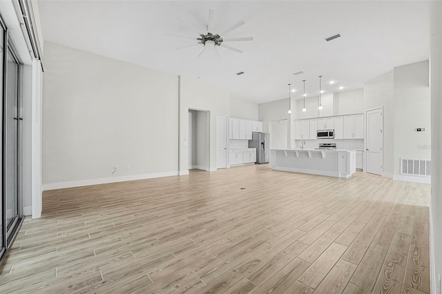 unfurnished living room featuring ceiling fan, light hardwood / wood-style flooring, and a high ceiling