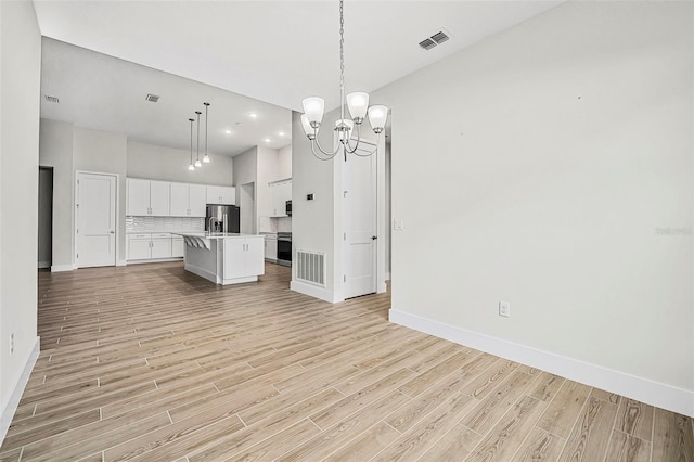 kitchen with pendant lighting, white cabinetry, decorative backsplash, a kitchen island with sink, and stainless steel refrigerator with ice dispenser