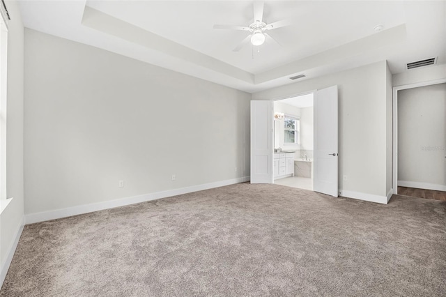 unfurnished bedroom featuring a raised ceiling, ensuite bathroom, and light carpet