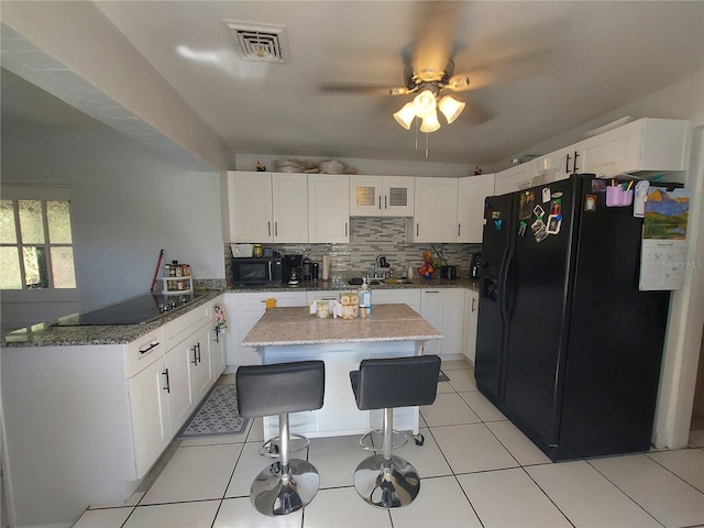 kitchen featuring a kitchen bar, white cabinetry, kitchen peninsula, dark stone counters, and black appliances