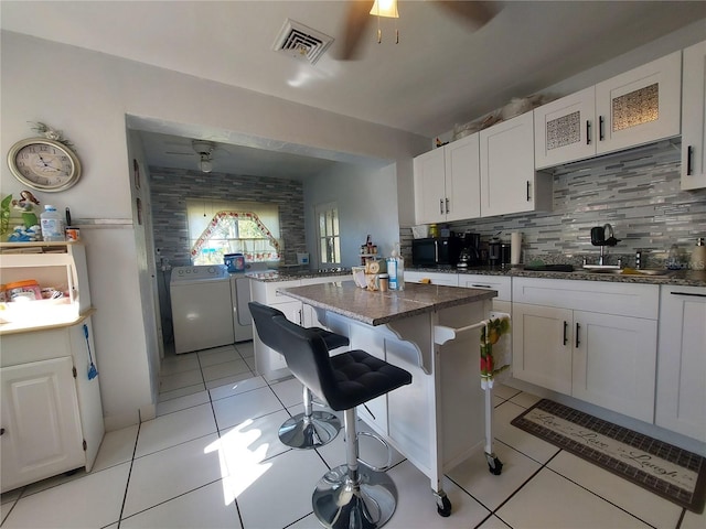 kitchen featuring white cabinetry, a kitchen breakfast bar, dark stone counters, a center island, and independent washer and dryer