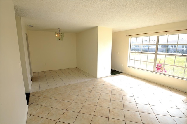 empty room with light tile patterned floors, a notable chandelier, and a textured ceiling