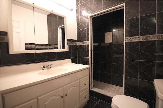 bathroom featuring a tile shower, tile walls, vanity, and toilet