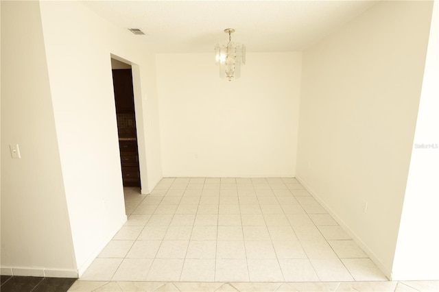 tiled spare room with a chandelier