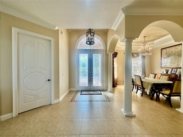 tiled entryway with decorative columns, a chandelier, crown molding, a textured ceiling, and french doors