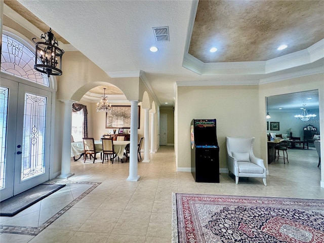 foyer featuring ornate columns, an inviting chandelier, a raised ceiling, crown molding, and a textured ceiling