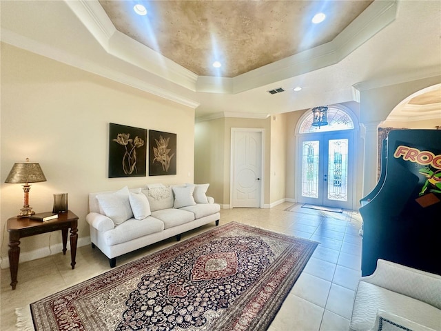 living room featuring light tile patterned flooring, french doors, crown molding, a tray ceiling, and decorative columns