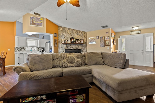 living room featuring lofted ceiling, hardwood / wood-style floors, a stone fireplace, and a textured ceiling