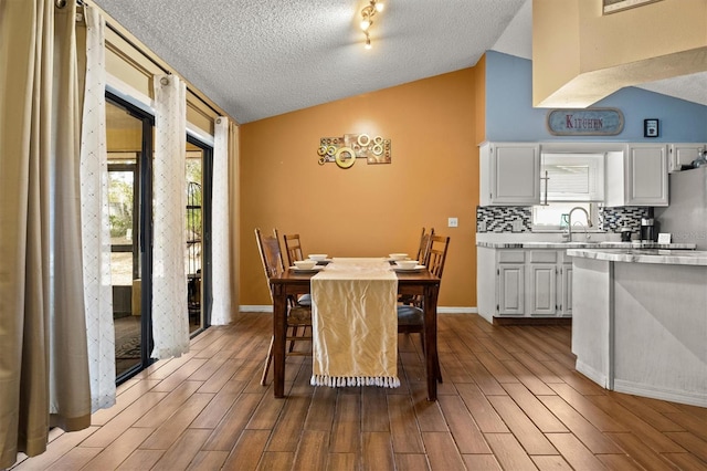 dining area with lofted ceiling, sink, a textured ceiling, and light wood-type flooring