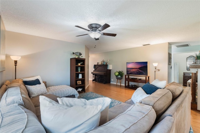 living room featuring ceiling fan, a fireplace, a textured ceiling, and light wood-type flooring