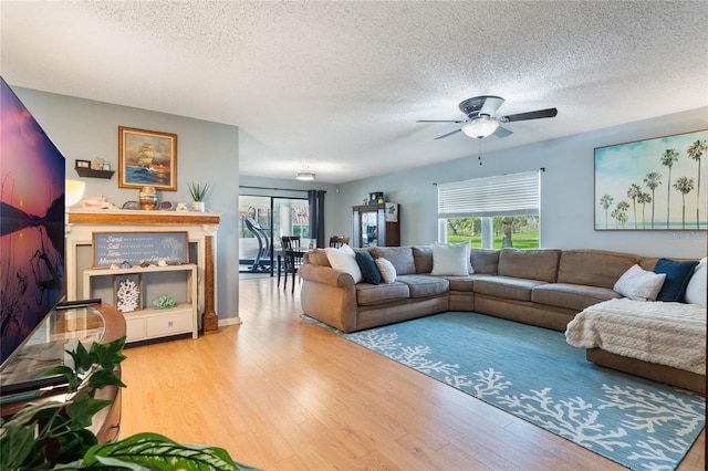 living room featuring ceiling fan, a textured ceiling, and light wood-type flooring