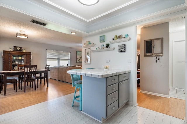 kitchen with tile countertops, light hardwood / wood-style floors, a textured ceiling, and a kitchen bar