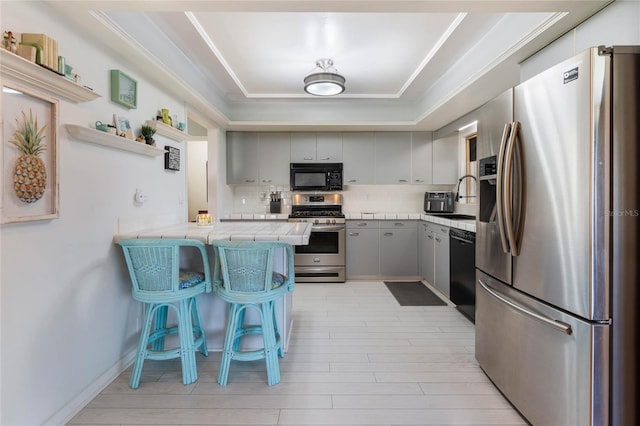 kitchen with a breakfast bar, kitchen peninsula, tasteful backsplash, black appliances, and a tray ceiling