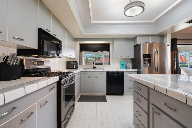 kitchen with tasteful backsplash, sink, tile counters, black appliances, and a raised ceiling