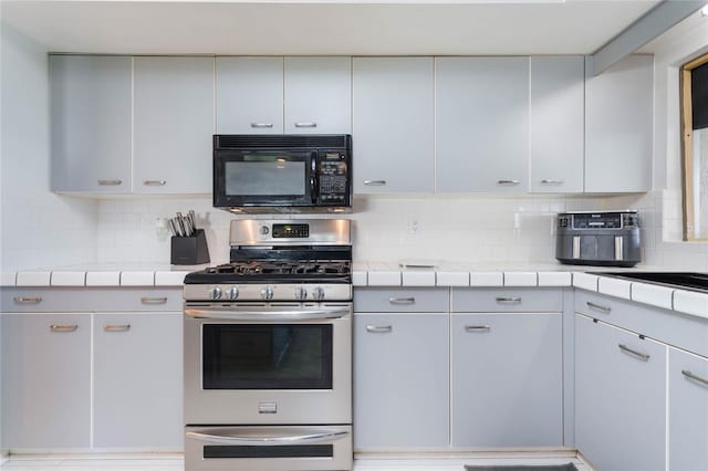 kitchen with tile counters, stainless steel range with gas stovetop, and backsplash