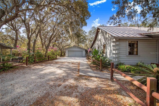 view of side of property featuring fence, a standing seam roof, an outdoor structure, a detached garage, and metal roof