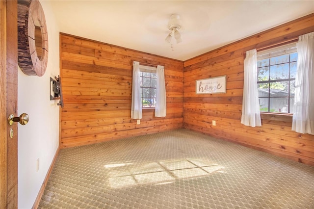 unfurnished room with a wealth of natural light, wooden walls, and carpet