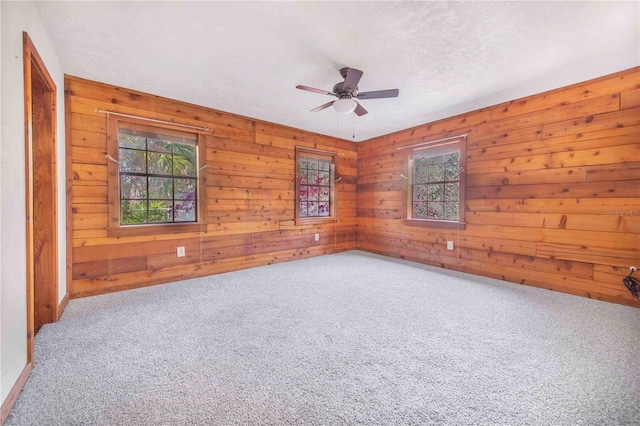 carpeted spare room featuring wooden walls and a ceiling fan