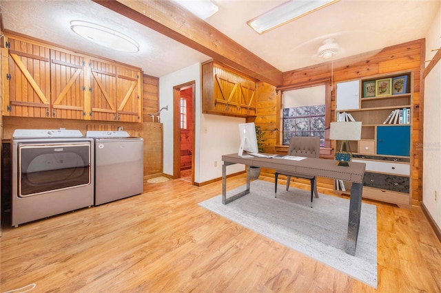 laundry area featuring light wood-type flooring, washing machine and dryer, cabinet space, wooden walls, and baseboards