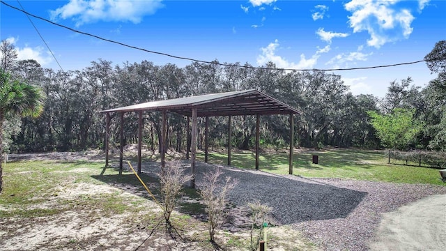 surrounding community featuring a detached carport, a lawn, a forest view, and gravel driveway