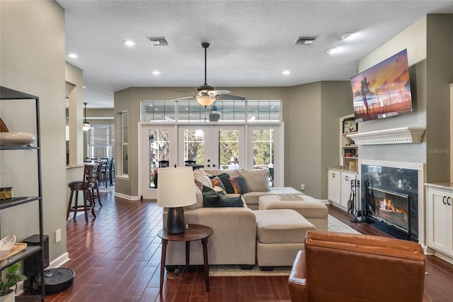 living room with a premium fireplace, ceiling fan, a textured ceiling, dark hardwood / wood-style flooring, and french doors