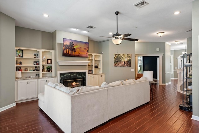 living room with dark wood-type flooring, ceiling fan, and a high end fireplace