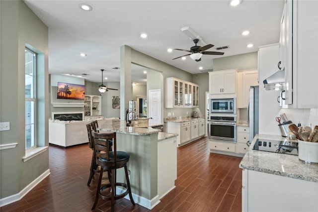 kitchen with appliances with stainless steel finishes, a kitchen island with sink, white cabinets, and a kitchen bar