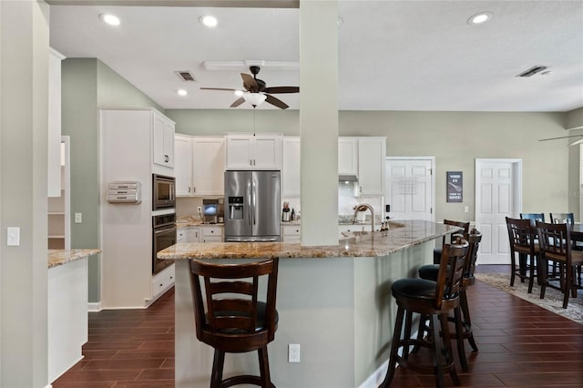 kitchen featuring stainless steel appliances, white cabinetry, light stone countertops, and a kitchen bar