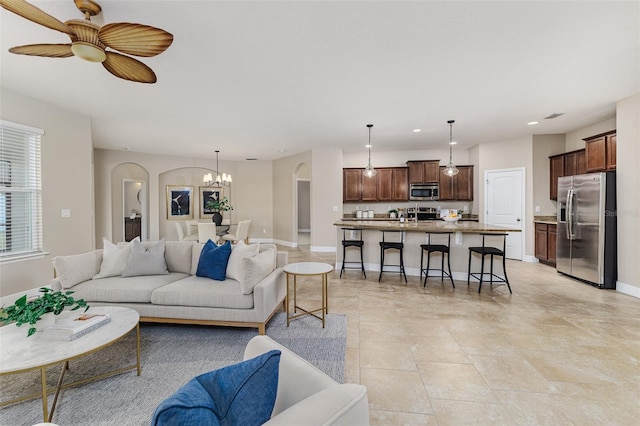 tiled living room with ceiling fan with notable chandelier