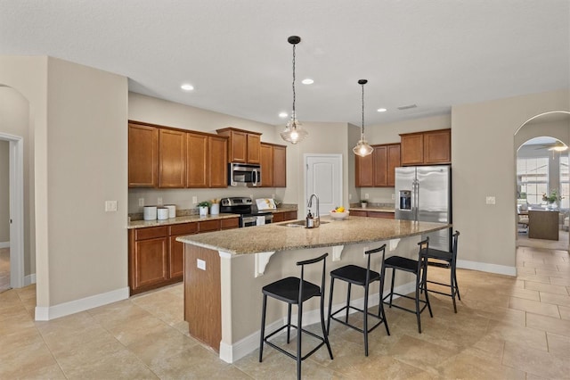 kitchen with a center island with sink, a kitchen breakfast bar, pendant lighting, stainless steel appliances, and light stone countertops