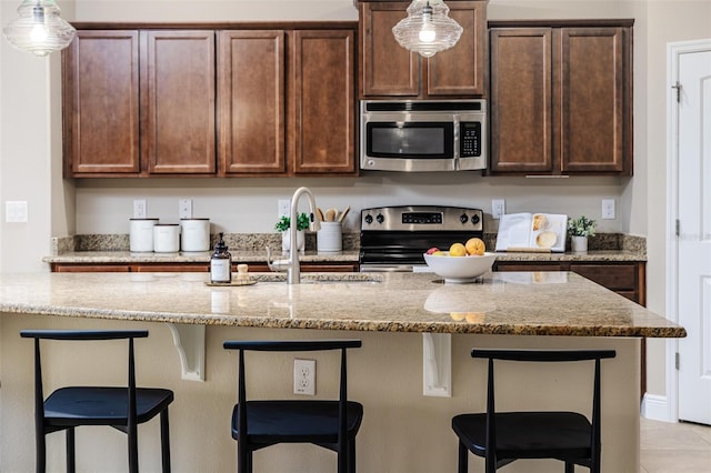 kitchen featuring decorative light fixtures, sink, a breakfast bar area, stainless steel appliances, and light stone countertops