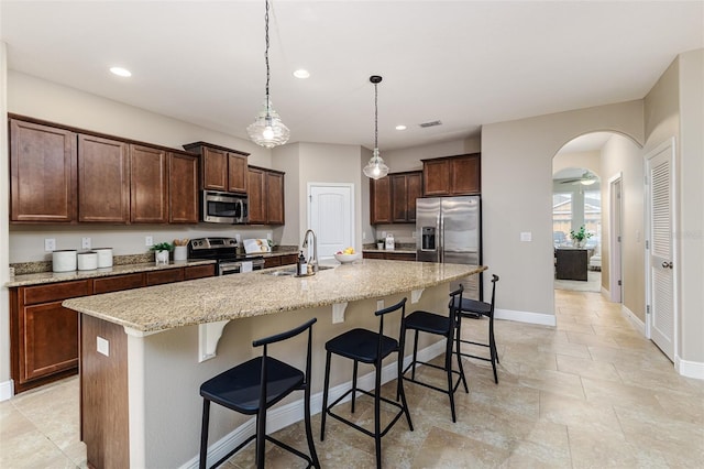 kitchen with sink, stainless steel appliances, a kitchen breakfast bar, light stone counters, and a center island with sink