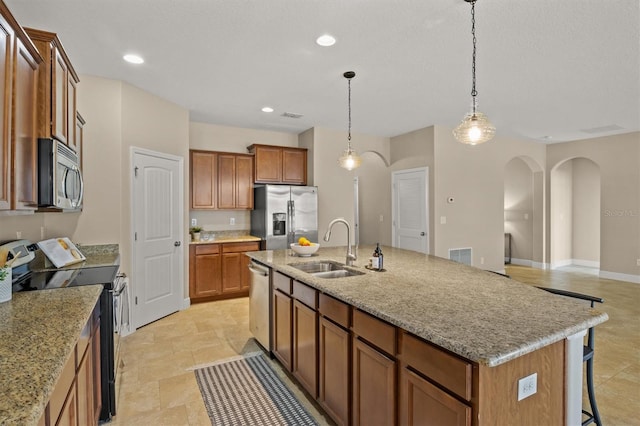 kitchen featuring pendant lighting, sink, stainless steel appliances, light stone countertops, and an island with sink