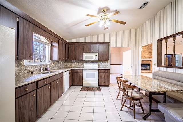 kitchen with dark brown cabinetry, sink, light tile patterned floors, white appliances, and a fireplace