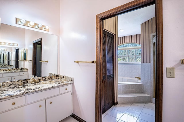 bathroom featuring a relaxing tiled tub, vanity, and tile patterned flooring