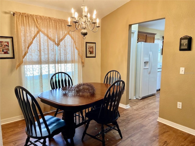 dining space with wood-type flooring, vaulted ceiling, and a notable chandelier