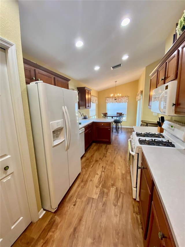 kitchen featuring lofted ceiling, white appliances, hanging light fixtures, a notable chandelier, and light hardwood / wood-style floors