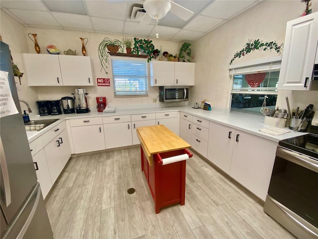 kitchen featuring sink, white cabinetry, stainless steel appliances, light hardwood / wood-style floors, and a drop ceiling