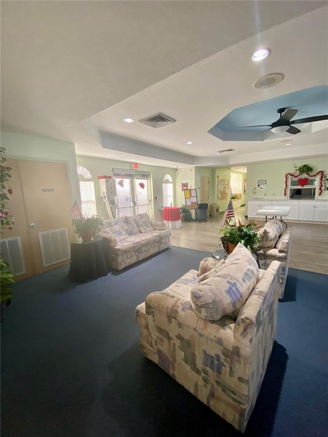 living room with a tray ceiling and ceiling fan