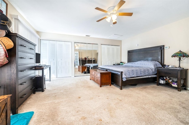 bedroom with ceiling fan, light colored carpet, and two closets