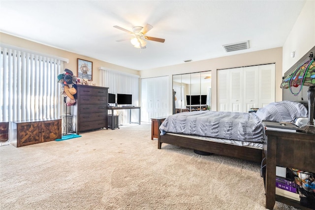 bedroom featuring ceiling fan, light colored carpet, and multiple closets