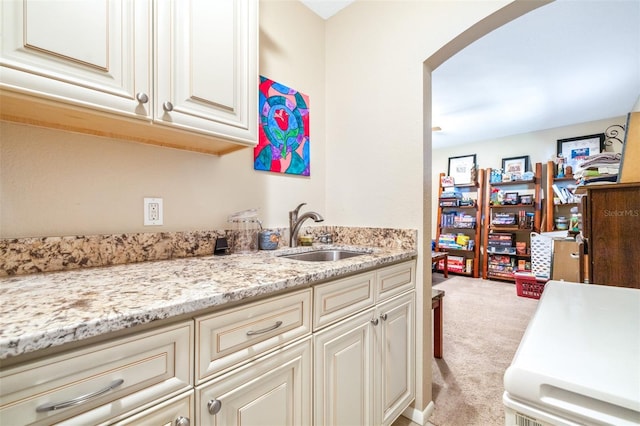 kitchen with light carpet, sink, light stone countertops, and cream cabinetry