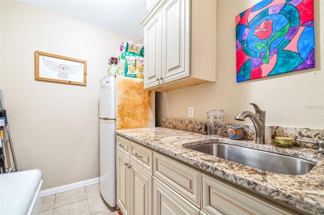 kitchen featuring white refrigerator, light tile patterned flooring, sink, and light stone counters