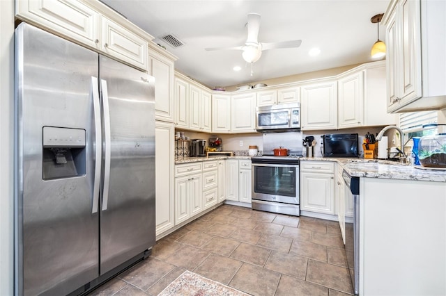 kitchen with sink, light stone counters, pendant lighting, ceiling fan, and stainless steel appliances