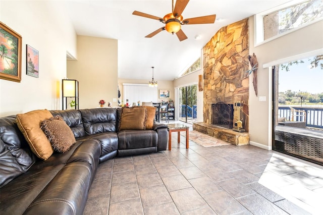 tiled living room featuring ceiling fan with notable chandelier, a fireplace, and high vaulted ceiling