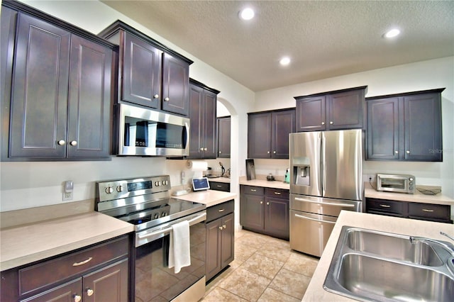 kitchen with dark brown cabinetry, stainless steel appliances, sink, and a textured ceiling