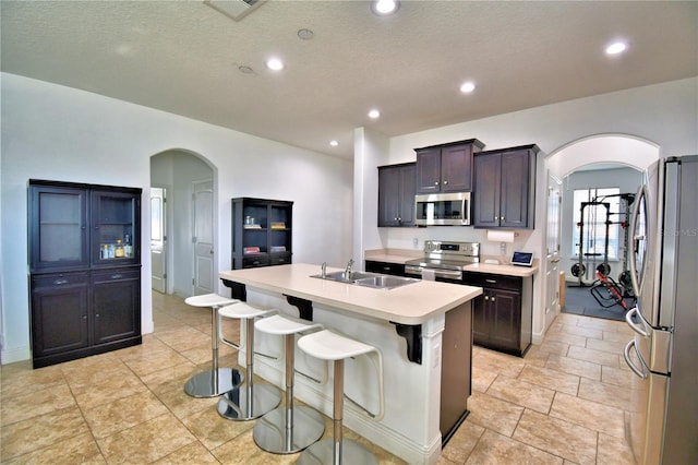 kitchen with sink, dark brown cabinets, stainless steel appliances, and an island with sink